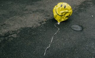 deflated balloon with a happy face on it, in the middle of the street