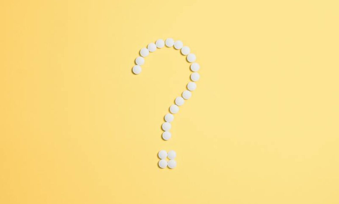 white medical pills in the shape of a question mark on a yellow background