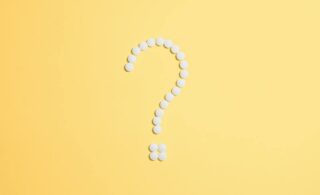 white medical pills in the shape of a question mark on a yellow background