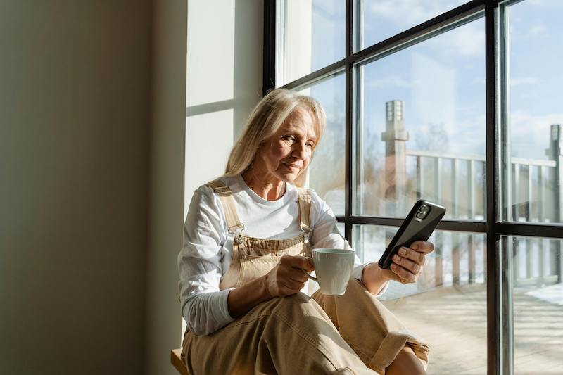 woman sitting in the window with a cup of tea and her phone
