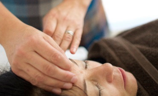 Close up of an acupuncturist's hands treating a patient, touching their forehead.
