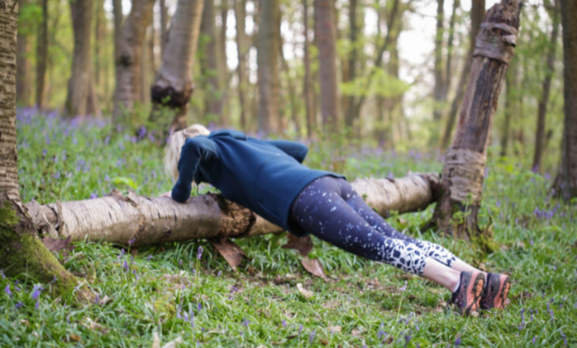 Bluebell wood with a blonde haired woman doing a push up against a fallen tree trun
