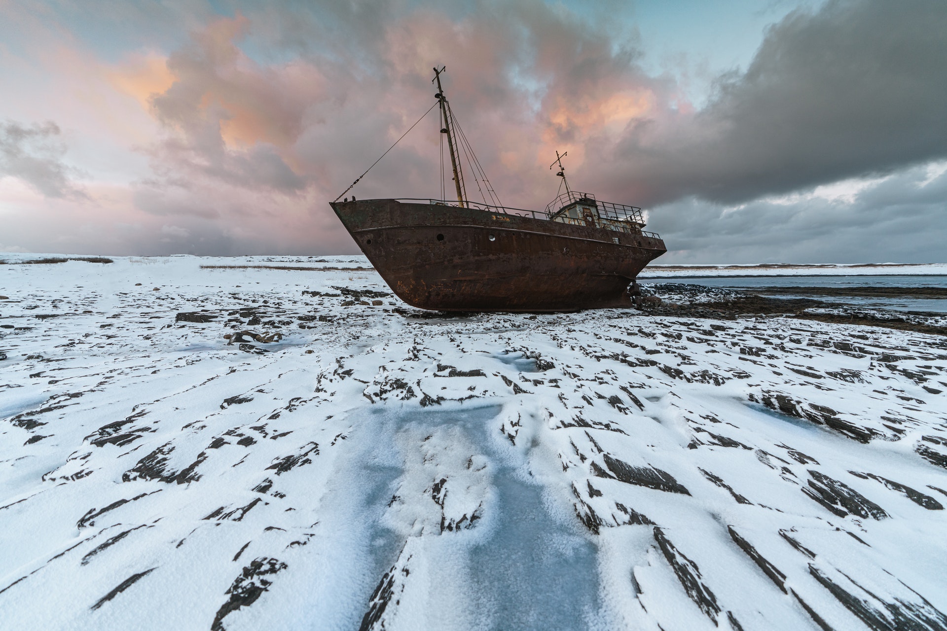 ship on frozen sea with grey, pink moody clouds in the background