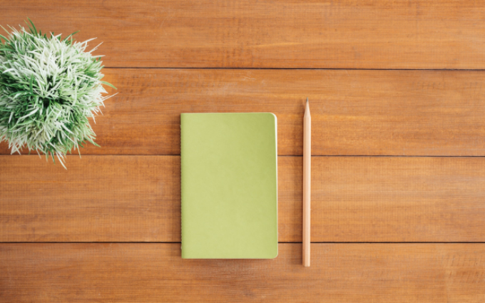 Birds eye view of green notebook on a wooden desk and cactus